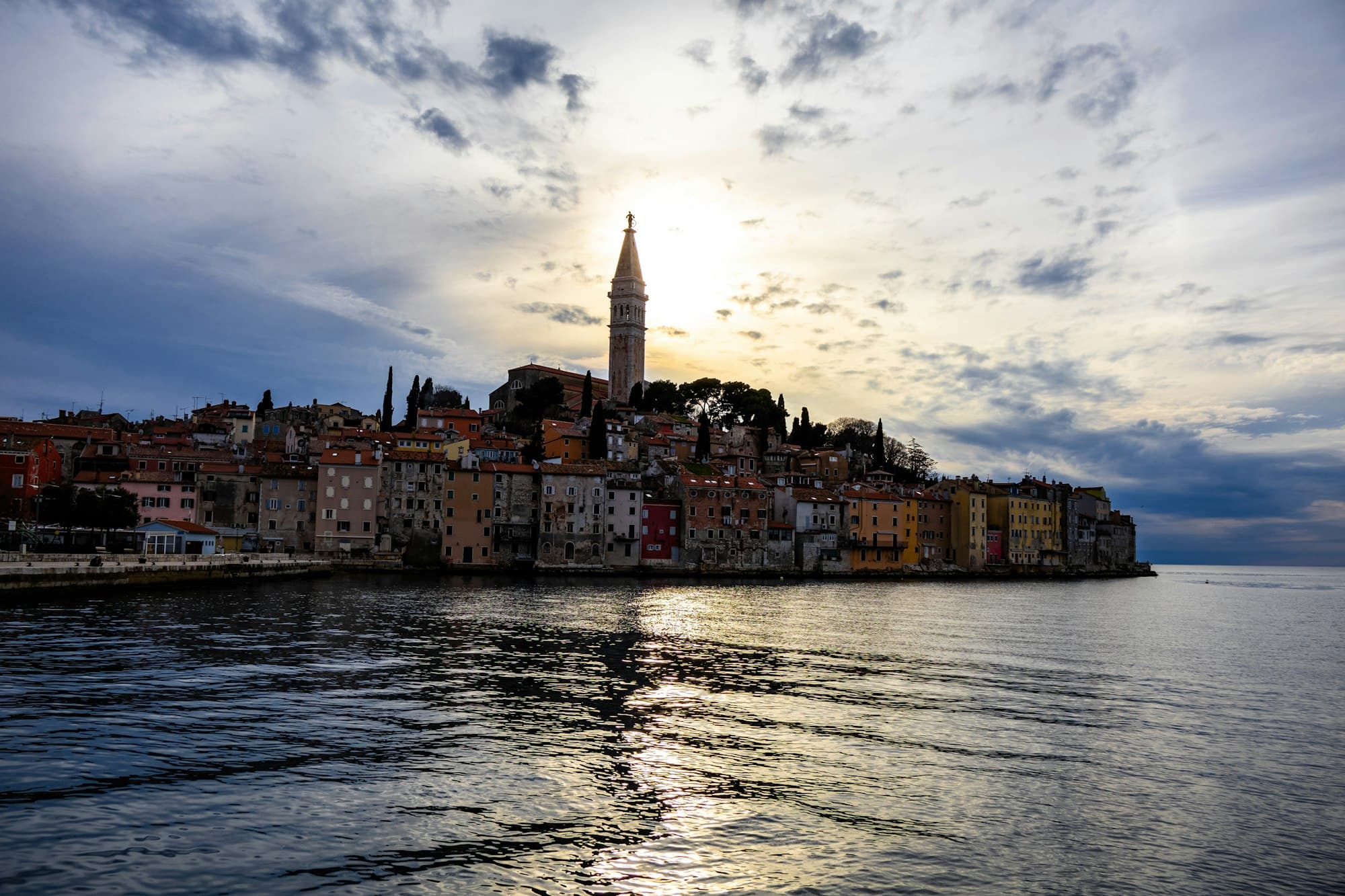 The Rovinj peninsula in silhouette at golden hour, the sun just behind the bell tower